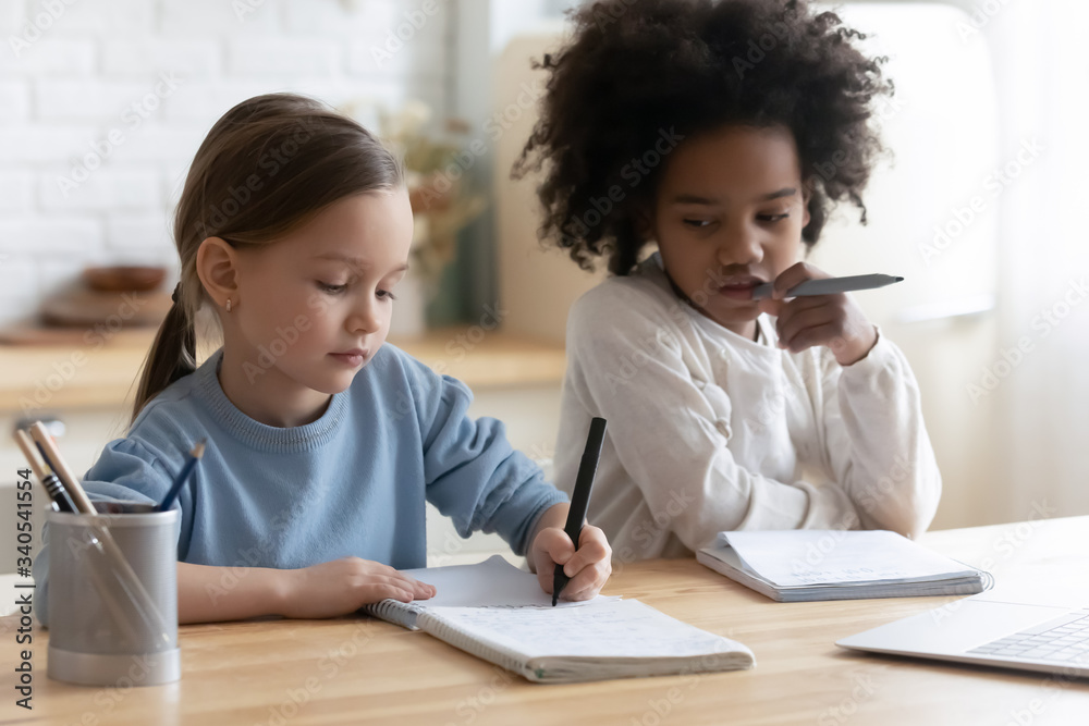 Small multiracial girls sisters sit at desk in kitchen study together using laptop, little multiethnic siblings prepare homework, have web online lesson or class on computer, homeschooling concept Small multiracial girls sisters sit at desk in kitchen study together using laptop, little multiethnic siblings prepare homework, have web online lesson or class on computer, homeschooling concept