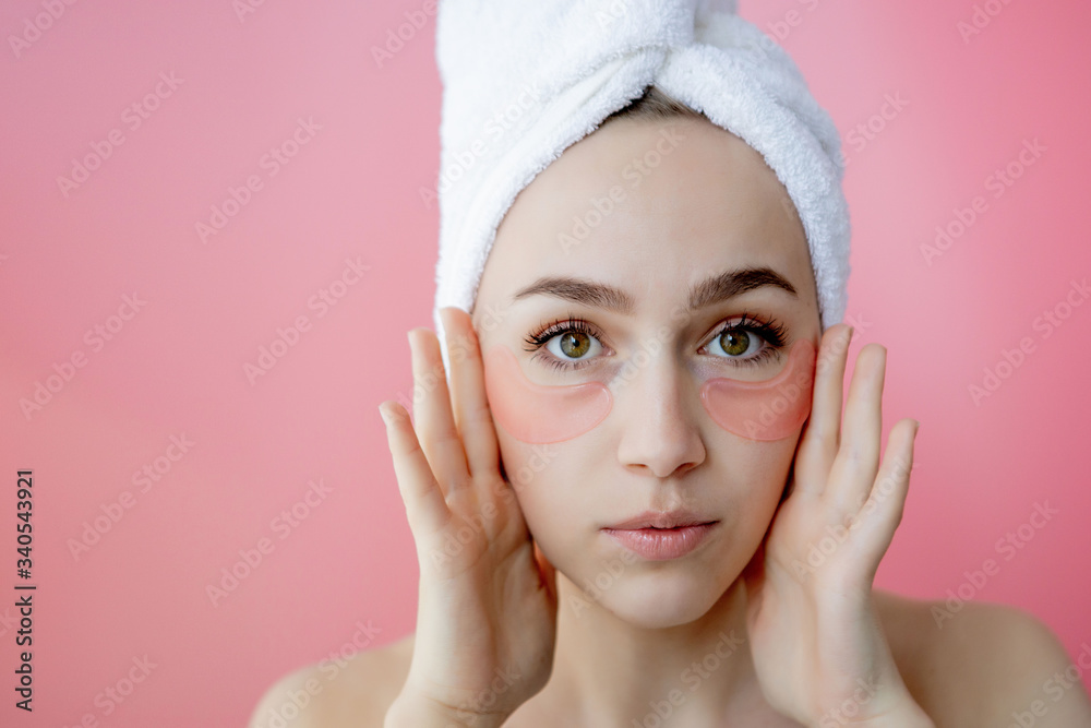 Studio shot of satisfied caucasian freckled woman wearing white towel on head, with collagen patches under eyes, standing naked against pink background. Skin care, cosmetic product concept Studio shot of satisfied caucasian freckled woman wearing white towel on head, with collagen patches under eyes, standing naked against pink background. Skin care, cosmetic product concept