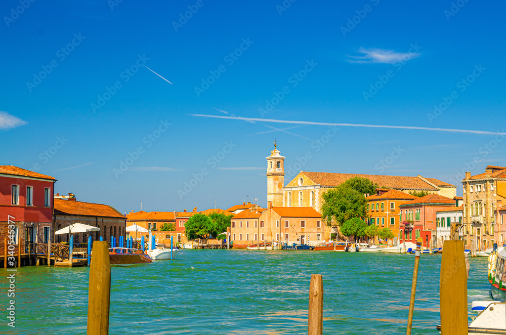 Murano islands water canal with Santa Maria degli Angeli church, boats and motor boats, row of traditional buildings, Venetian Lagoon, Veneto Region, Northern Italy. Murano postcard cityscape.