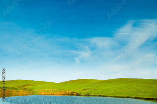 Green meadow with lake and hills and cloudy sky