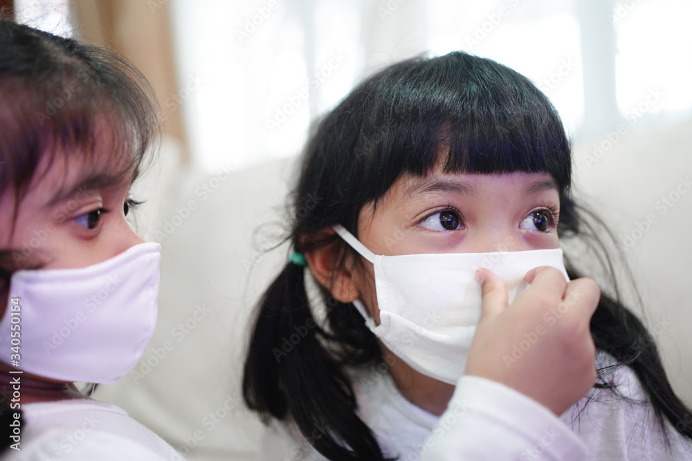 Sister helping her younger sister to wear the medical surgical mask to protect from virus, sickness, Covid-19 and coronavirus infection.