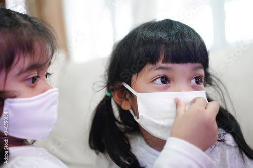 Sister helping her younger sister to wear the medical surgical mask to protect from virus, sickness, Covid-19 and coronavirus infection.