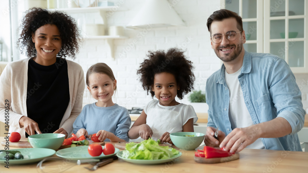 Portrait of happy young multiracial family with little children cook together in modern renovated kitchen, smiling multiethnic parents have fun preparing healthy food breakfast with small daughters Portrait of happy young multiracial family with little children cook together in modern renovated kitchen, smiling multiethnic parents have fun preparing healthy food breakfast with small daughters