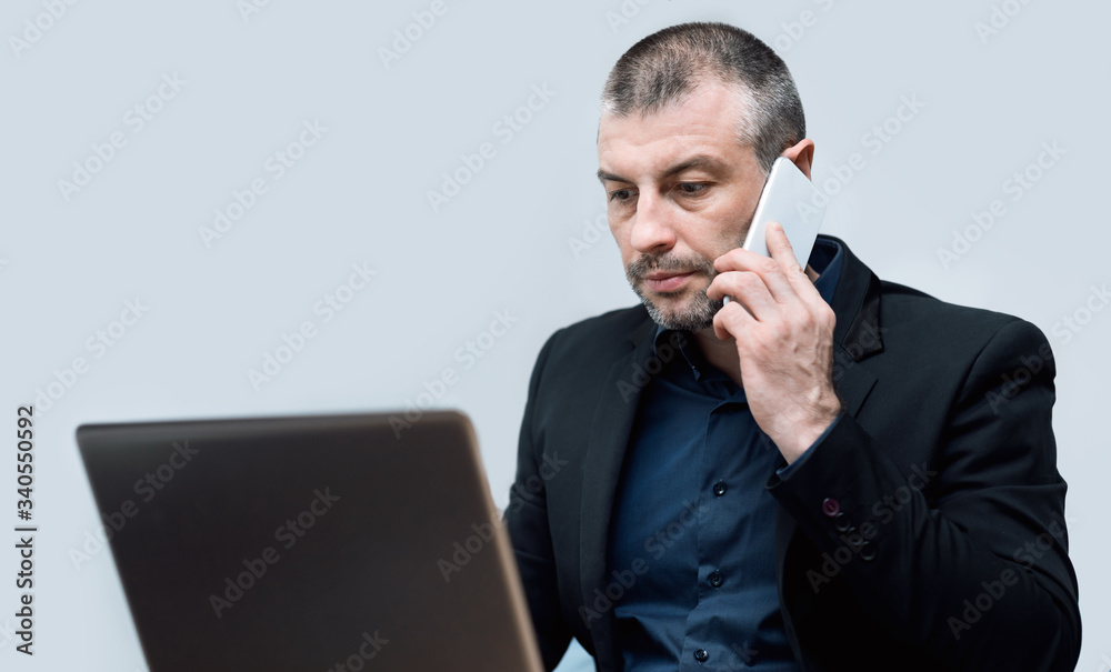 Entrepreneur Talking On Cellphone Working On Laptop Sitting, Gray Background Entrepreneur Talking On Cellphone Working On Laptop Sitting, Gray Background