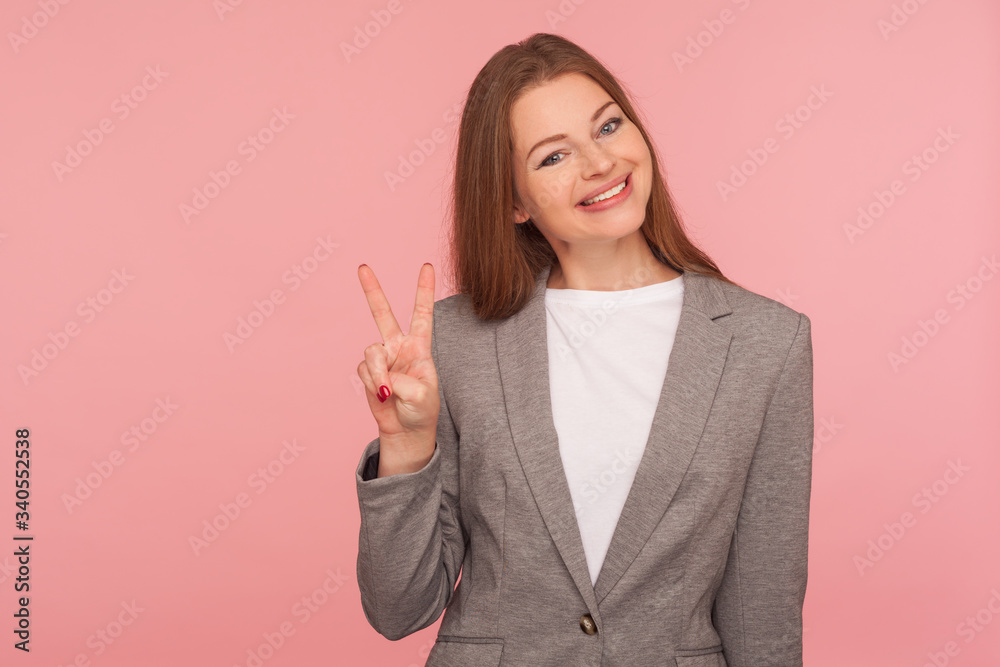 Portrait of positive young woman in business suit smiling and showing victory gesture, making double v sign, enjoying successful startup, job promotion. studio shot isolated on pink background Portrait of positive young woman in business suit smiling and showing victory gesture, making double v sign, enjoying successful startup, job promotion. studio shot isolated on pink background