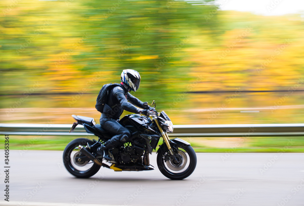 Single biker on a motorcycle with motion blurred background. Driving on a street in front of a blurred autumn tree.
