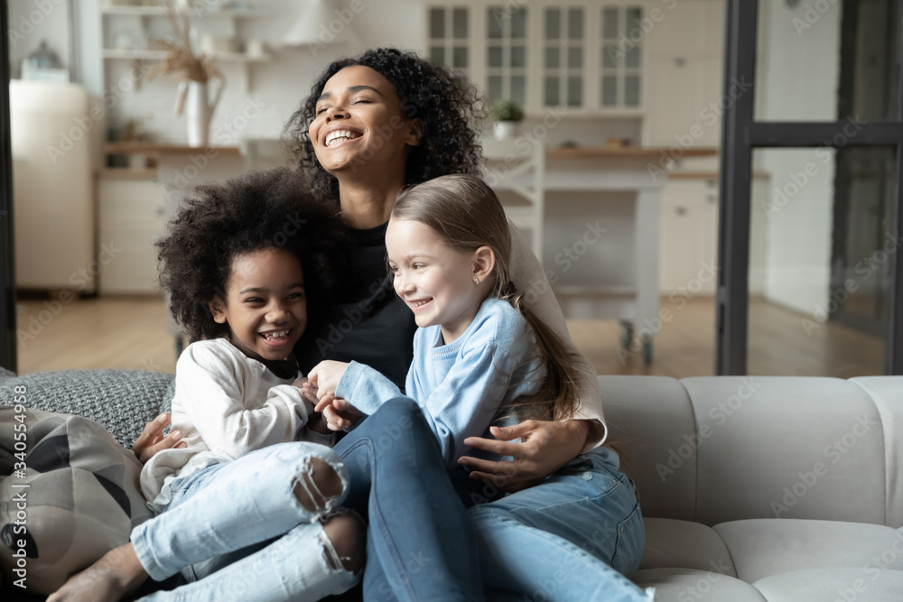 Overjoyed young African American mother play with little multiracial daughters at home, happy biracial mom sit on couch tickle have fun with smiling small multiethnic girls kids on weekend together Overjoyed young African American mother play with little multiracial daughters at home, happy biracial mom sit on couch tickle have fun with smiling small multiethnic girls kids on weekend together