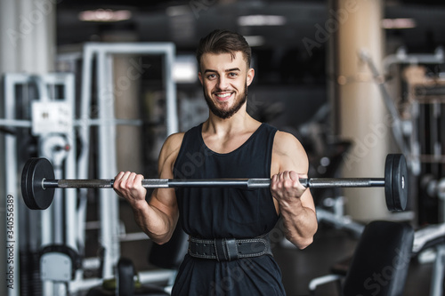 Strong man, bodybuilder in sportwear with dumbbells in a gym, exercising with a barbell