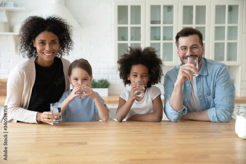 Portrait of happy young multiracial family with little kids drinking pure clean mineral water at home, smiling multiethnic parents with small daughters children recommend healthy lifestyle Portrait of happy young multiracial family with little kids drinking pure clean mineral water at home, smiling multiethnic parents with small daughters children recommend healthy lifestyle