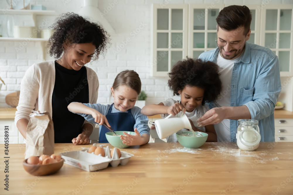 Happy young multiracial parents and little biracial daughters have fun baking in kitchen together, overjoyed family with cute small multiethnic children cooking in modern home preparing breakfast Happy young multiracial parents and little biracial daughters have fun baking in kitchen together, overjoyed family with cute small multiethnic children cooking in modern home preparing breakfast