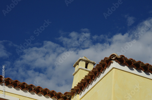 Detail of a house with roof and chimney and blue sky background © Enrico Spetrino