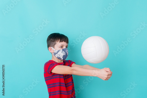 Boy with a mask due to the corona virus play volleyball on blue background. Workout online concept.