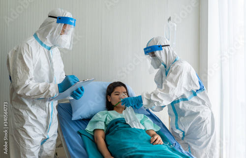 doctor and nurse in personal protective equipment or ppe giving oxygen mask with bag to the asian woman patient with covid-19 or coronavirus infection in hospital during pandemic photo