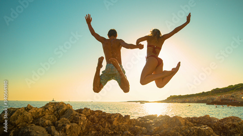 LOW ANGLE: Cheerful young couple holds hands while diving into ocean at sunset