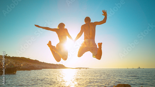 Sticker LENS FLARE: Carefree tourists hold hands while jumping into the refreshing sea