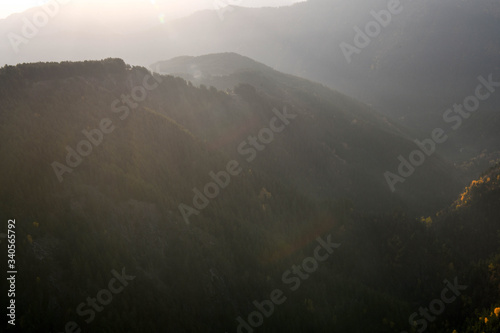 A mountainside with a forest is lit by the rising sun in the Tusheti region.
