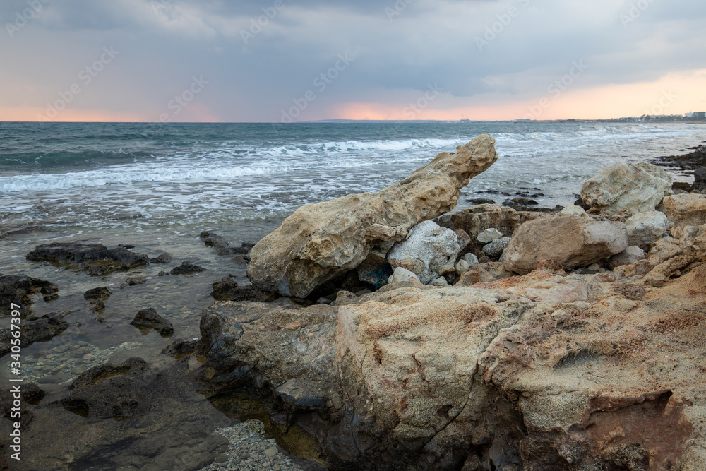 rocky sea coast at sunset, waves breaking on the rocks, small pools formed by nature in the rocks with a reflection of the dark sunset sky before a thunderstorm