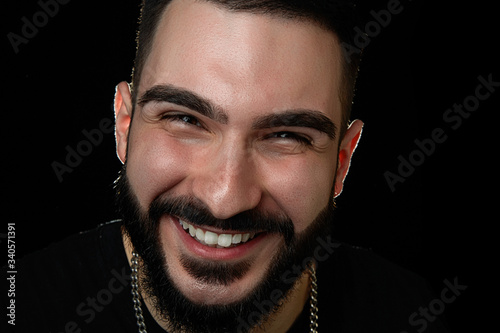 close-up of a dramatic portrait of a smiling young guy, a musician, singer, rapper with a beard in black clothes . on a black isolated background.