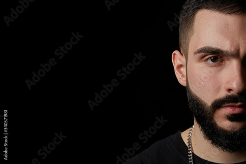 Carta da parati close-up of a dramatic portrait of a young serious guy, a musician, singer, rapper with a beard in black clothes