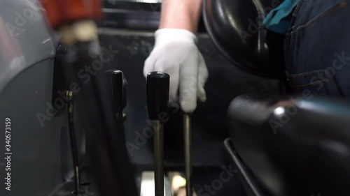 A man, operator, driver in white gloves controls the levers of the attachment of the hydraulic system of a small agricultural tractor. Harvesting, sowing. Agricultural technology. Collective farms.