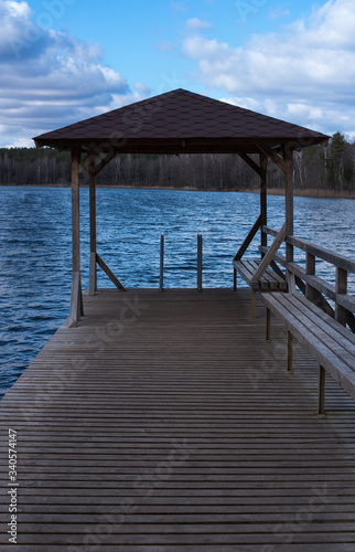 An empty tranquil bridge on a lake with a roof at the end on a cloudy but warm day
