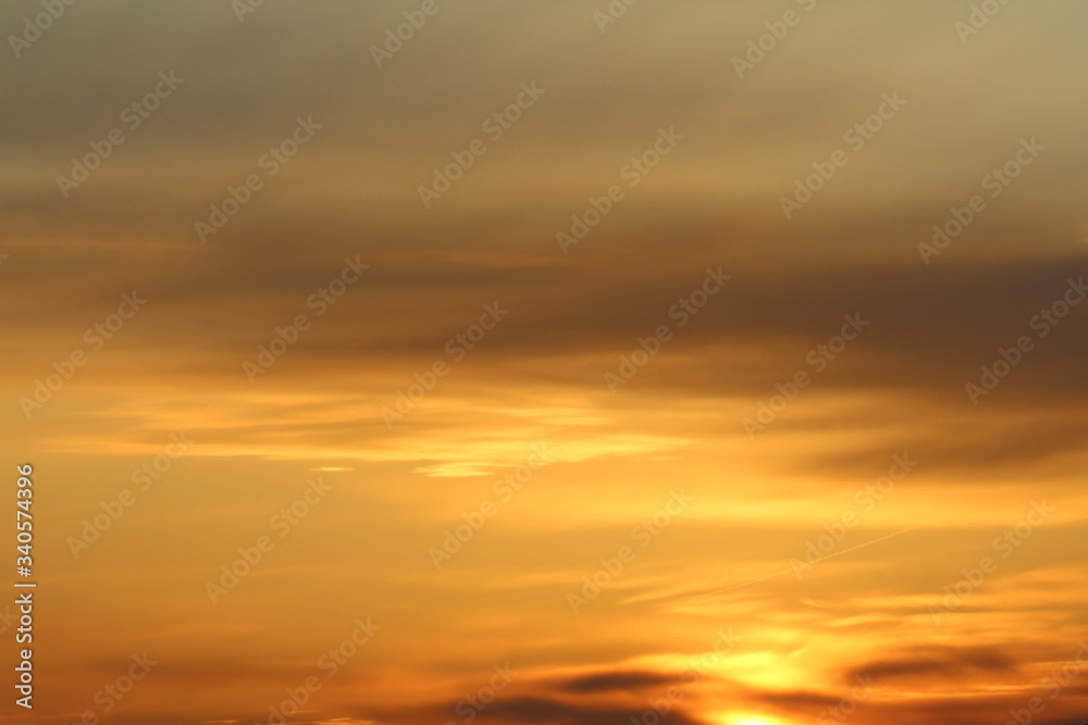 Sun below the horizon and clouds in the fiery dramatic orange sky at sunset or dawn backlit by the sun. Place for text and design.