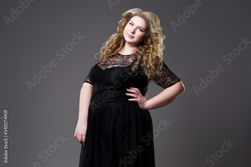 Plus size fashion model in black dress, fat woman on gray background