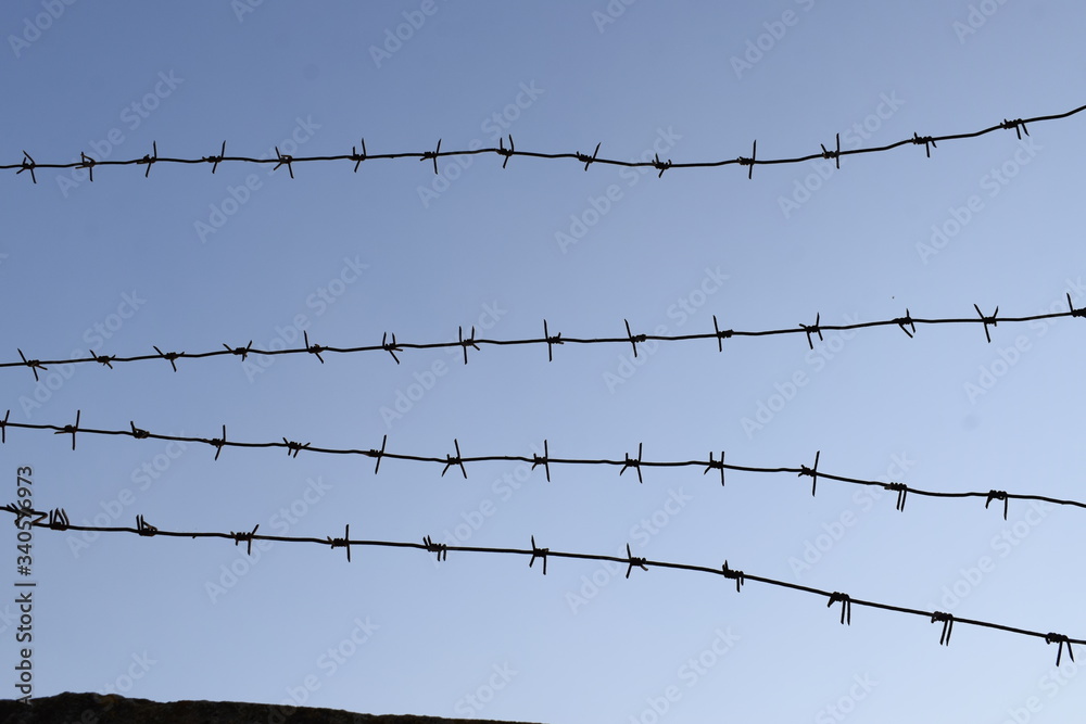 Barbed wire on a concrete fence against a blue sky. Barbed wire on a concrete fence against a blue sky.