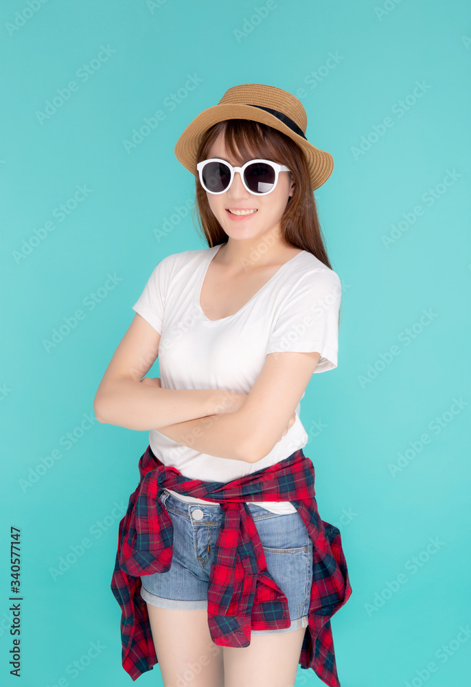 Fototapeta premium Beautiful portrait young asian woman wear hat and sunglasses smiling expression confident enjoy summer in vacation isolated on blue background, girl cheerful wear fashion travel concept.