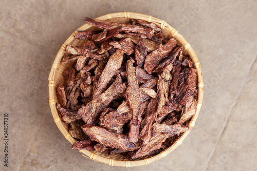 Top view on dehydrated homemade pet beef lungs chips in straw pot on stone background. Dog and cat chewy jerky and treats. Outdoors, close up, soft selective focus, copy space.