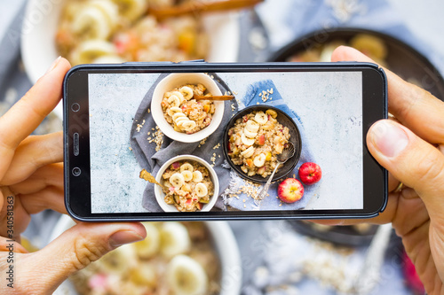 Make phone picture of food. Smartphone photo of fruits oatmeal porridge . Create blogging content. Vegan breakfast meal. Overhead.