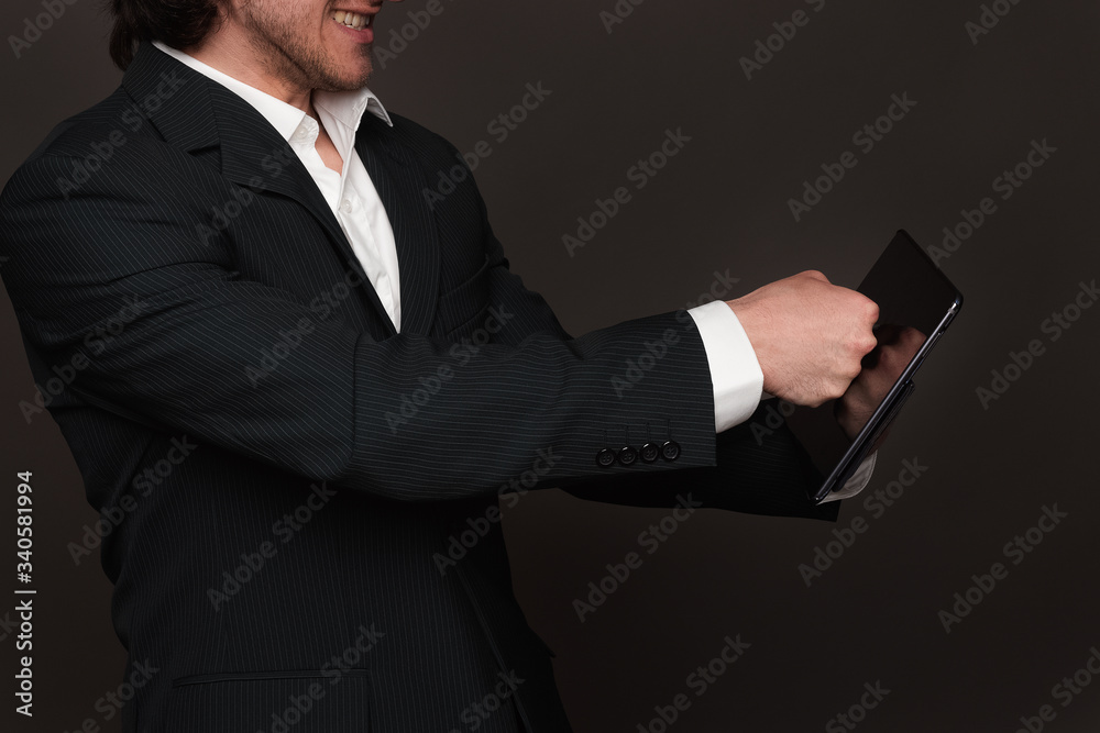 Businessman in black suit holding tablet pc on left palm and breaking screen with his fist. Bad deal, unsuccessful transaction, show of force Businessman in black suit holding tablet pc on left palm and breaking screen with his fist. Bad deal, unsuccessful transaction, show of force