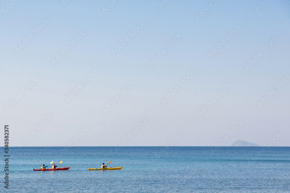 three kayakers in blue sea of Santorini, Greece
