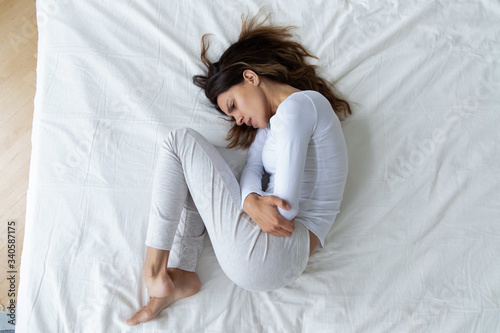 Papier peint Top view stressed unhappy young woman lying in fetal position on bed alone, feel