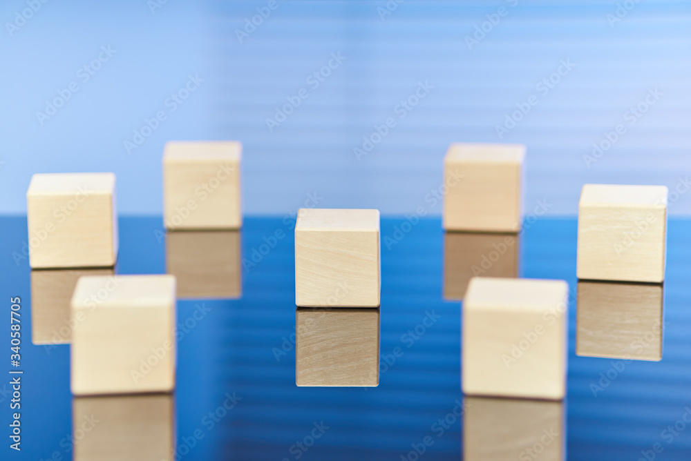 Seven wooden cubes on a blue background with a reflection on the surface. There is a visual emphasis on the cube in the center. Free space for letters, numbers, symbols, or labels. Seven wooden cubes on a blue background with a reflection on the surface. There is a visual emphasis on the cube in the center. Free space for letters, numbers, symbols, or labels.