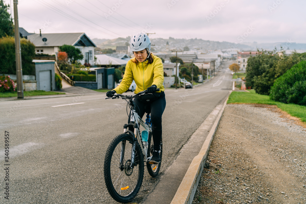 18/04/2020 Asian woman making uphill with mountain bike. A woman very tired and stop on street At Oamaru, New Zealand.