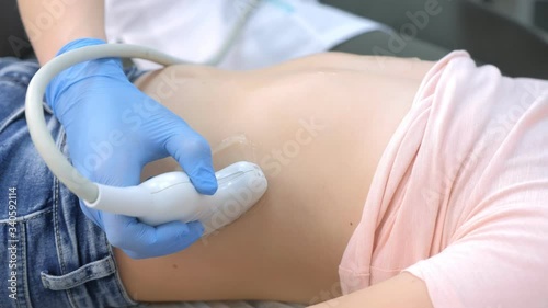 Doctor making abdominal ultrasound for child girl using scanner, closeup view, tummy and hands closeup. Woman runs ultrasound sensor over patient belly. Diagnostic examination of internal organs.