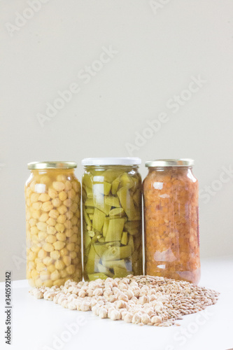Photo of non-perishable food purchased due to Covid-19, chickpeas, lentils, and green beans in jars and spilled on a white wooden board. Photo of in front of food cans and spilled food.