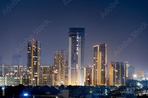 High rise multi story skyscrapers lit up at night with small houses in the foreground at night in gurgaon delhi