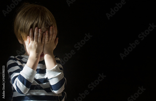 Foto Little Caucasians blond boy child 3-4 years old covered his face with his hands alone in the dark and is afraid