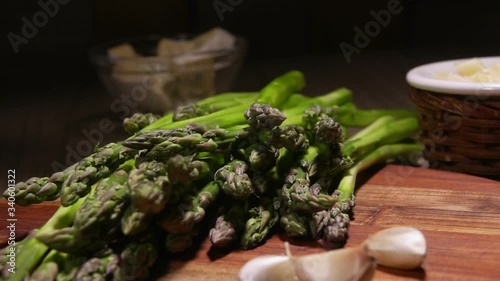 Peeled green asparagus spear falls on the bunch of asparagus on a wooden board next to tha garlic and cheese photo