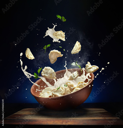 Hot pierogi flying out of the clay bowl with cream and parsley. Some vareniki stay inside the plate.  Green background. Blue background.