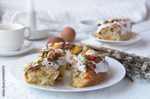 sweet bread with white icing, nuts and candied fruits lies on a plate, pastries