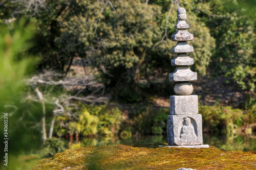 Single Japanese Buddhist stupa made of local stones stands on small islet. Oriental stupa is in the middle of a pond surrounded by natural forest. Symbol of peace and calm for East Asia people