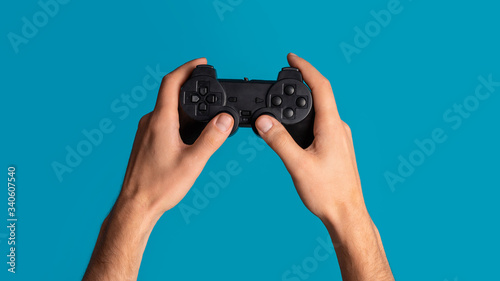 Lockdown activities. Millennial man holding video game controller on blue background, closeup. Panorama
