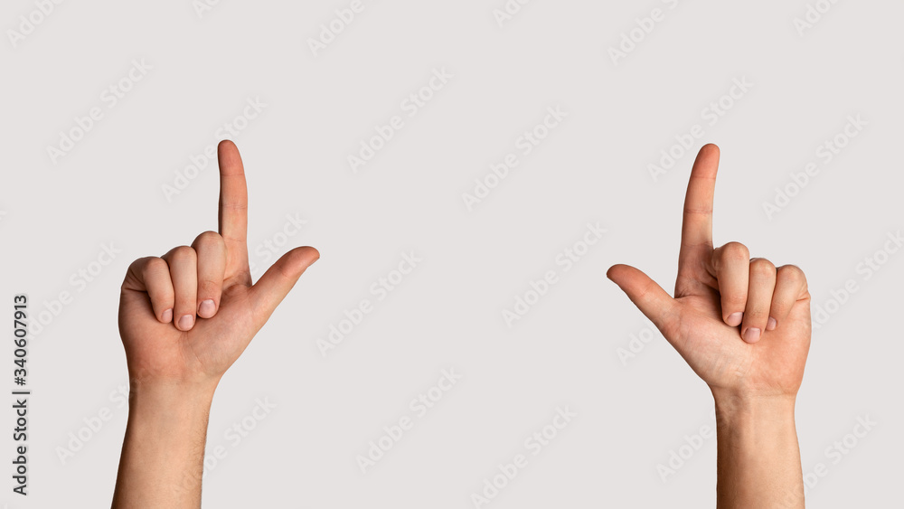 Close up of young male pointing upwards with both hands on light background, copy space. Panorama Close up of young male pointing upwards with both hands on light background, copy space. Panorama