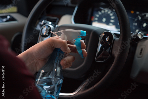 Hand of woman is spraying alcohol,disinfectant spray on steering wheel in her car,prevent infection of Covid-19 virus,contamination of germs or bacteria,wipe clean surfaces that are frequently touched © Evghenii Blanaru