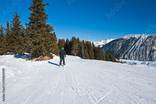 Skier on piste through trees in alpine resort