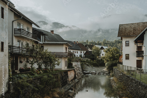 River and houses of Slovenian town Bohinjska Bistrica under the Julian Alps hiding in clouds in the background during the sunrise during the summer morning