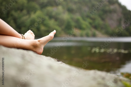 girl relaxing barefoot on rock by lake